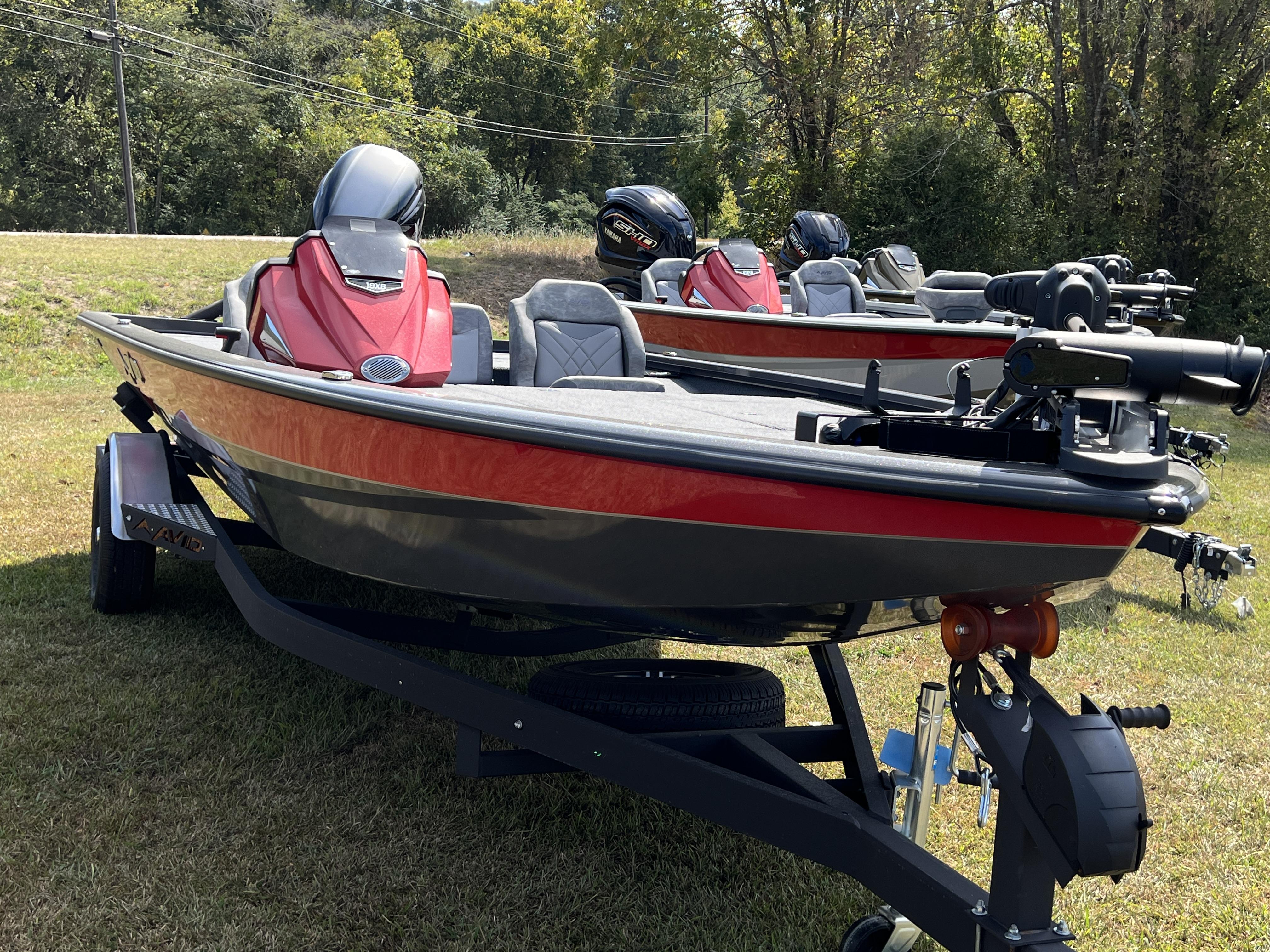 Slide: The Image of 2023 Avid 19XB fishing boats on trailers in a grassy area. - 1
