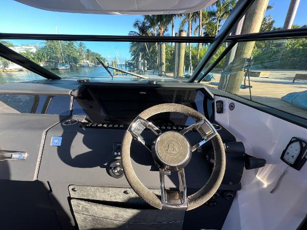 Slide: The Image of 2023 Axopar 37 Sun-Top helm with steering wheel and dashboard, docked near palm trees. - 49