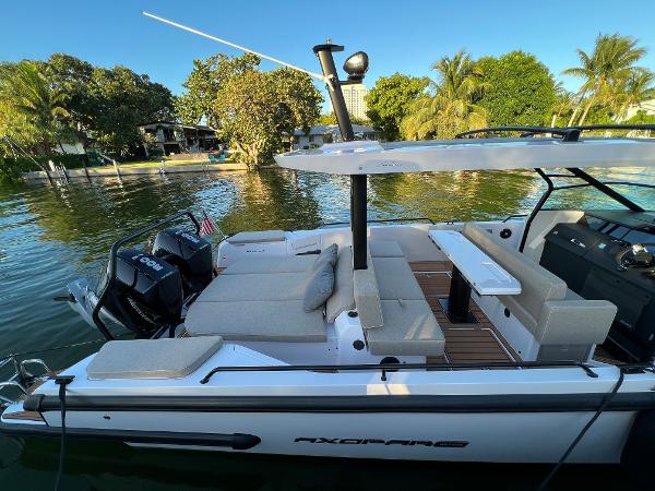 Slide: The Image of 2023 Axopar 37 Sun-Top boat docked on a serene lake with lush greenery. - 6
