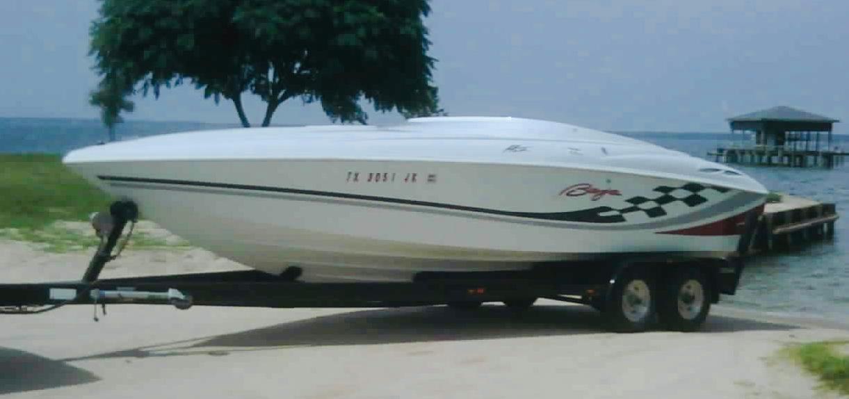 Slide: The Image of 2000 Baja H2X speedboat on trailer by lakeside, featuring sleek design and checkered graphics. - 1