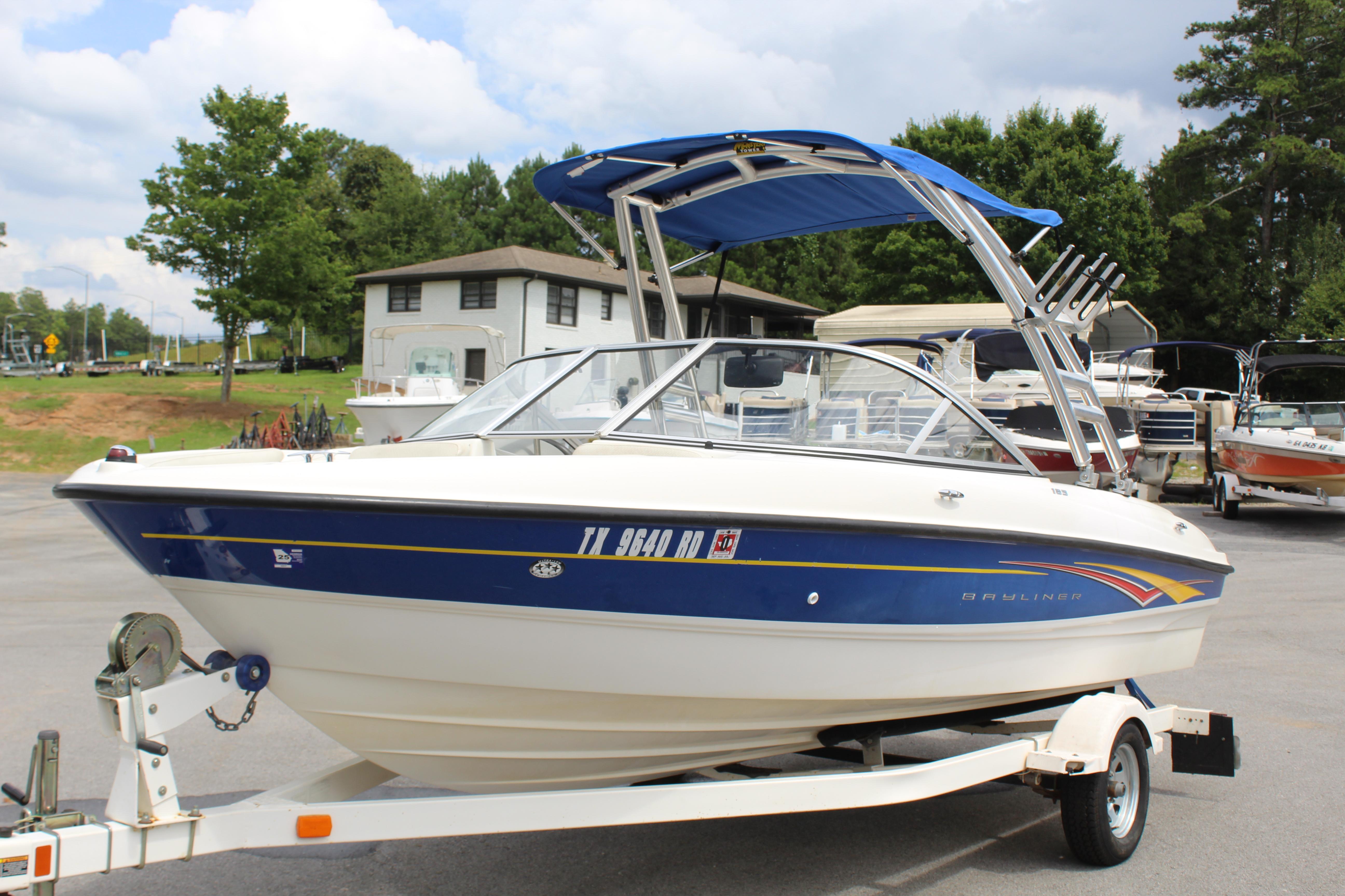 Slide: The Image of 2007 Bayliner 185 Bowrider boat on trailer, parked outdoors with trees and buildings in background. - 2