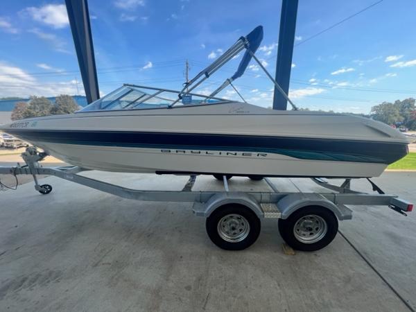 Slide: The Image of 1995 Bayliner 2050 Capri boat on trailer, under a canopy, with blue sky background. - 1