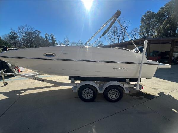 Slide: The Image of 2018 Bayliner 210 Deck Boat on trailer, parked outdoors under clear blue sky. - 1