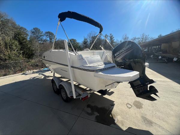 Slide: The Image of 2018 Bayliner 210 Deck Boat with Mercury engine on trailer, parked outdoors. - 2
