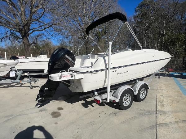 Slide: The Image of 2018 Bayliner 210 Deck Boat on trailer, parked outdoors, with outboard motor. - 3