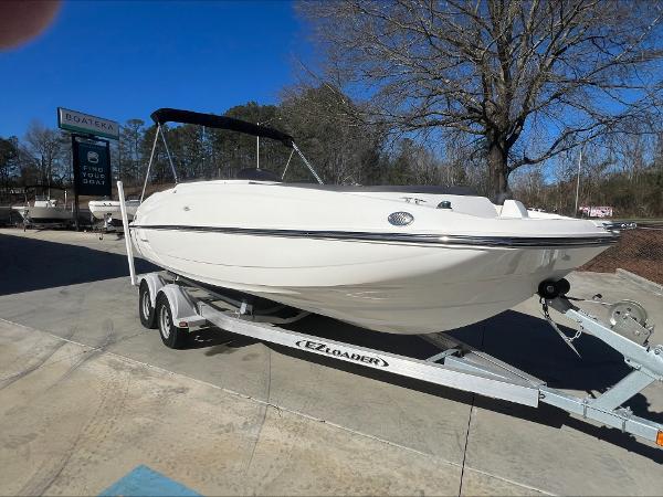 Slide: The Image of 2018 Bayliner 210 Deck Boat on trailer, parked outdoors under clear blue sky. - 5