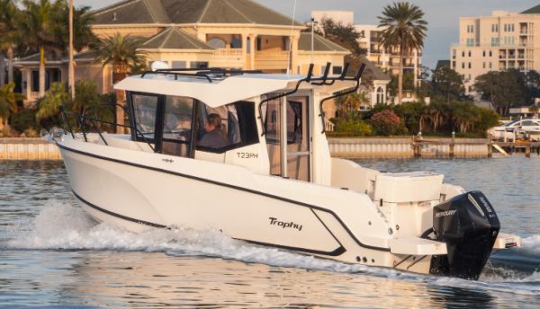 Slide: The Image of 2024 Bayliner Trophy 23 Pilothouse boat cruising on water near waterfront homes. - 25