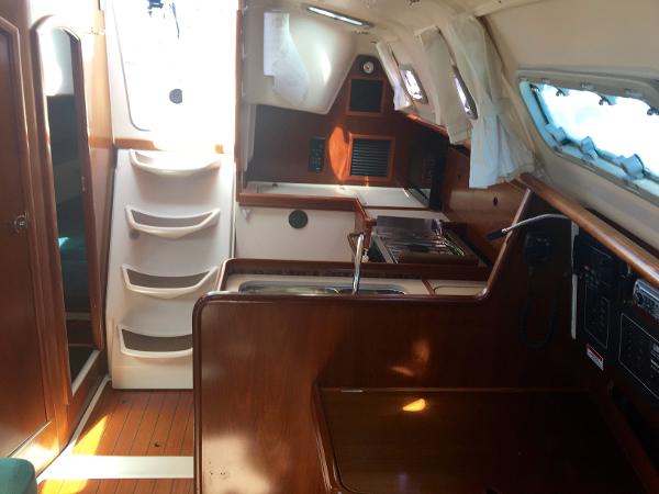 Slide: The Image of Interior of 2000 Beneteau Oceanis 321 sailboat, featuring wood finishes and compact kitchen area. - 34