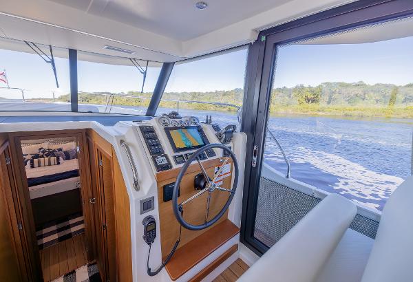 Slide: The Image of 2021 Beneteau Swift Trawler 41 helm with navigation equipment, overlooking serene waters. - 16