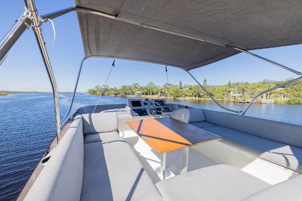 Slide: The Image of 2021 Beneteau Swift Trawler 41 flybridge with seating, table, and canopy on a scenic waterway. - 48
