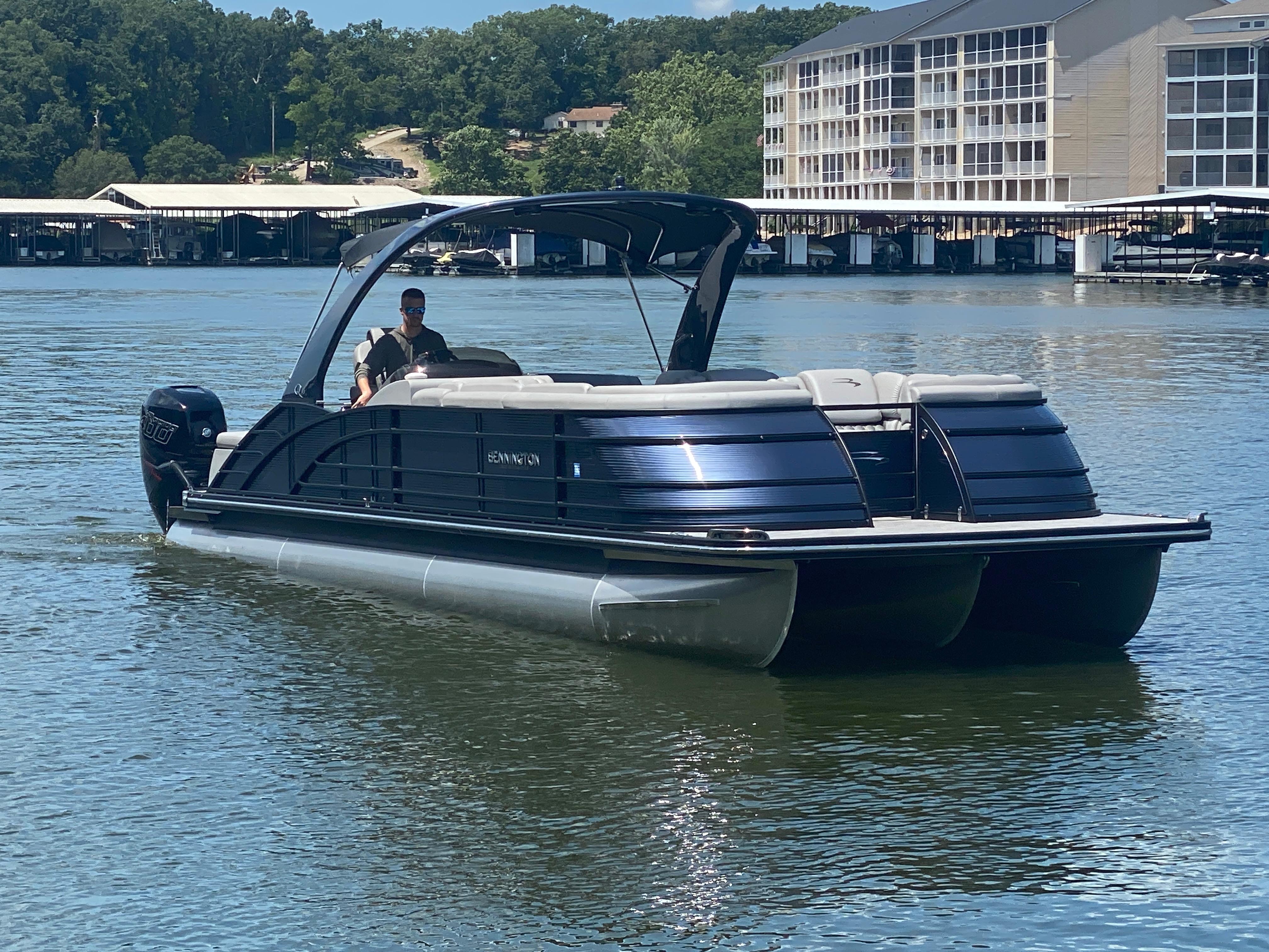 Slide: The Image of 2020 Bennington 30 QSBAX2 pontoon boat cruising on a lake near a marina. - 0