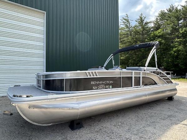 Slide: The Image of 2022 Bennington L25 pontoon boat parked outdoors near a green building. - 1