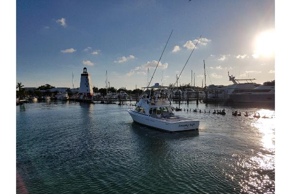 Slide: The Image of 2023 Bertram 35 Flybridge boat cruising in a marina at sunset with a lighthouse in the background. - 38