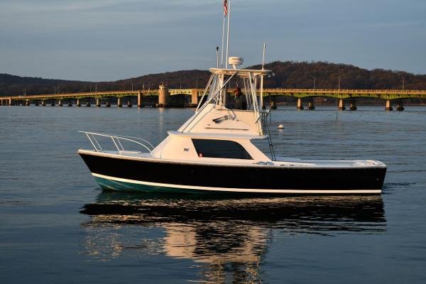 Slide: The Image of 1965 Bertram Sportfisher boat on calm water near a bridge at sunset. - 1