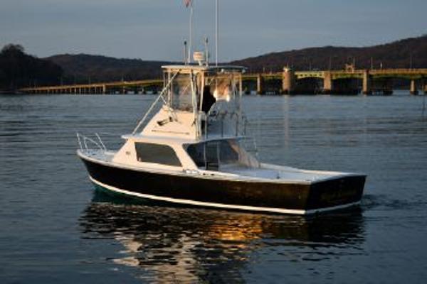 Slide: The Image of 1965 Bertram Sportfisher boat on calm water near a bridge at sunset. - 2
