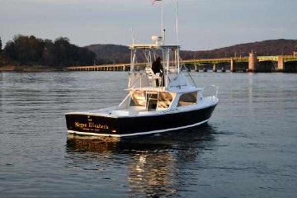 Slide: The Image of 1965 Bertram Sportfisher boat on calm water near a bridge and wooded shoreline. - 4