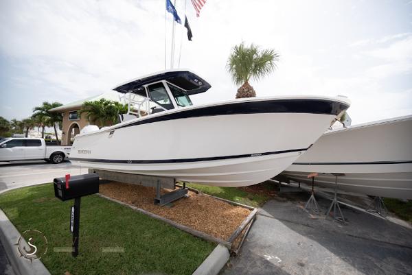 Slide: The Image of 2024 Blackfin 272 CC boat displayed outdoors with flags and palm trees. - 1
