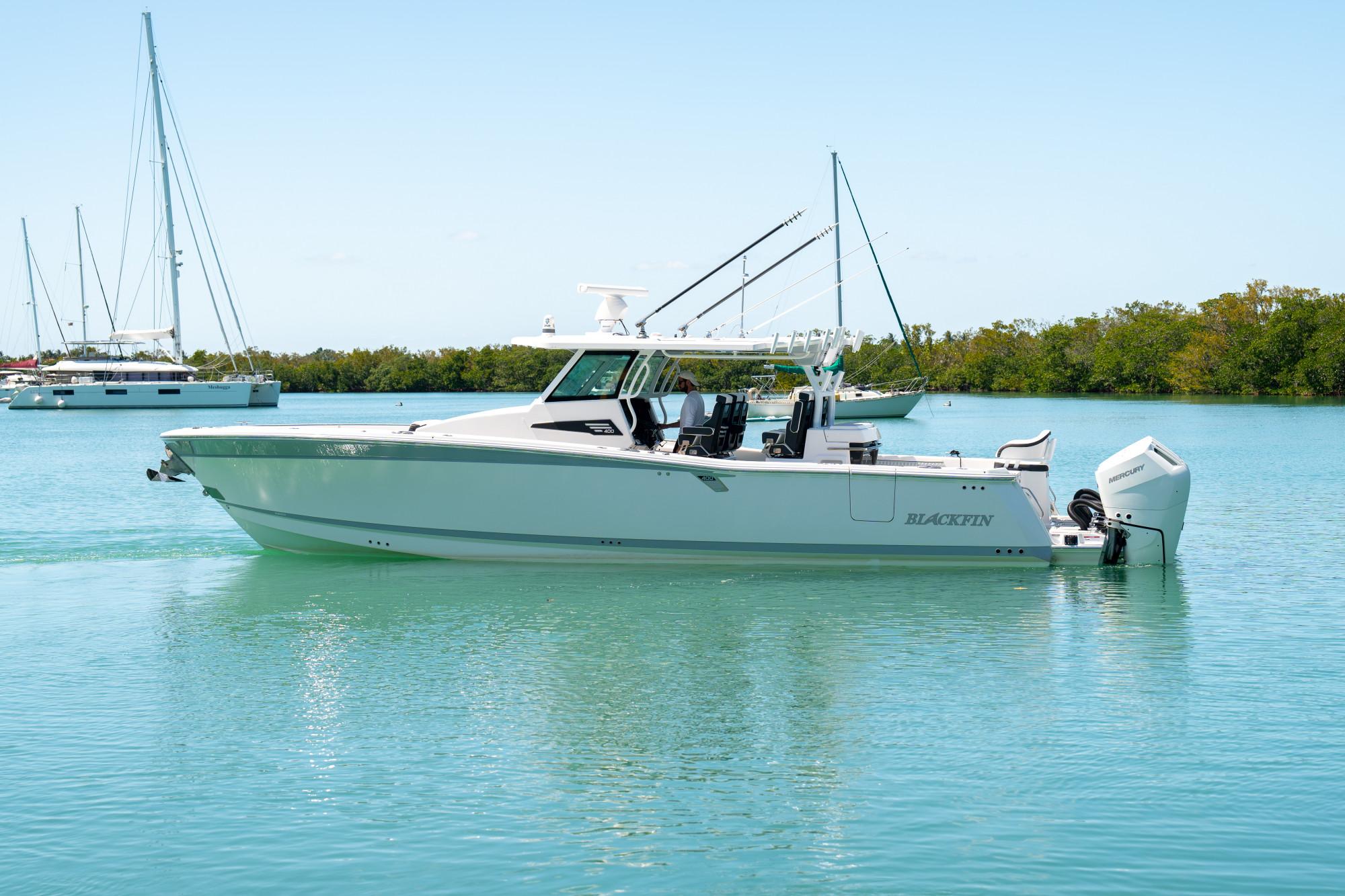 Slide: The Image of 2024 Blackfin 400 CC boat on calm water, surrounded by sailboats and greenery. - 6