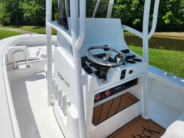 Slide: The Image of 2025 BlackJack 256 Coastal boat console with steering wheel, set against a lush green backdrop. - 15
