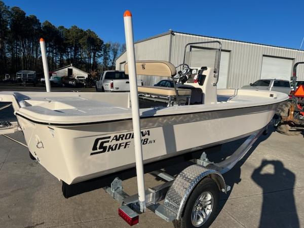 Slide: The Image of 2025 Carolina Skiff E18 CC boat on trailer, parked outdoors near a warehouse. - 3