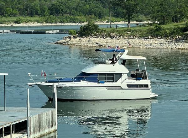 Slide: The Image of 1994 Carver 350 Aft Cabin yacht on a serene lake with lush green surroundings. - 0