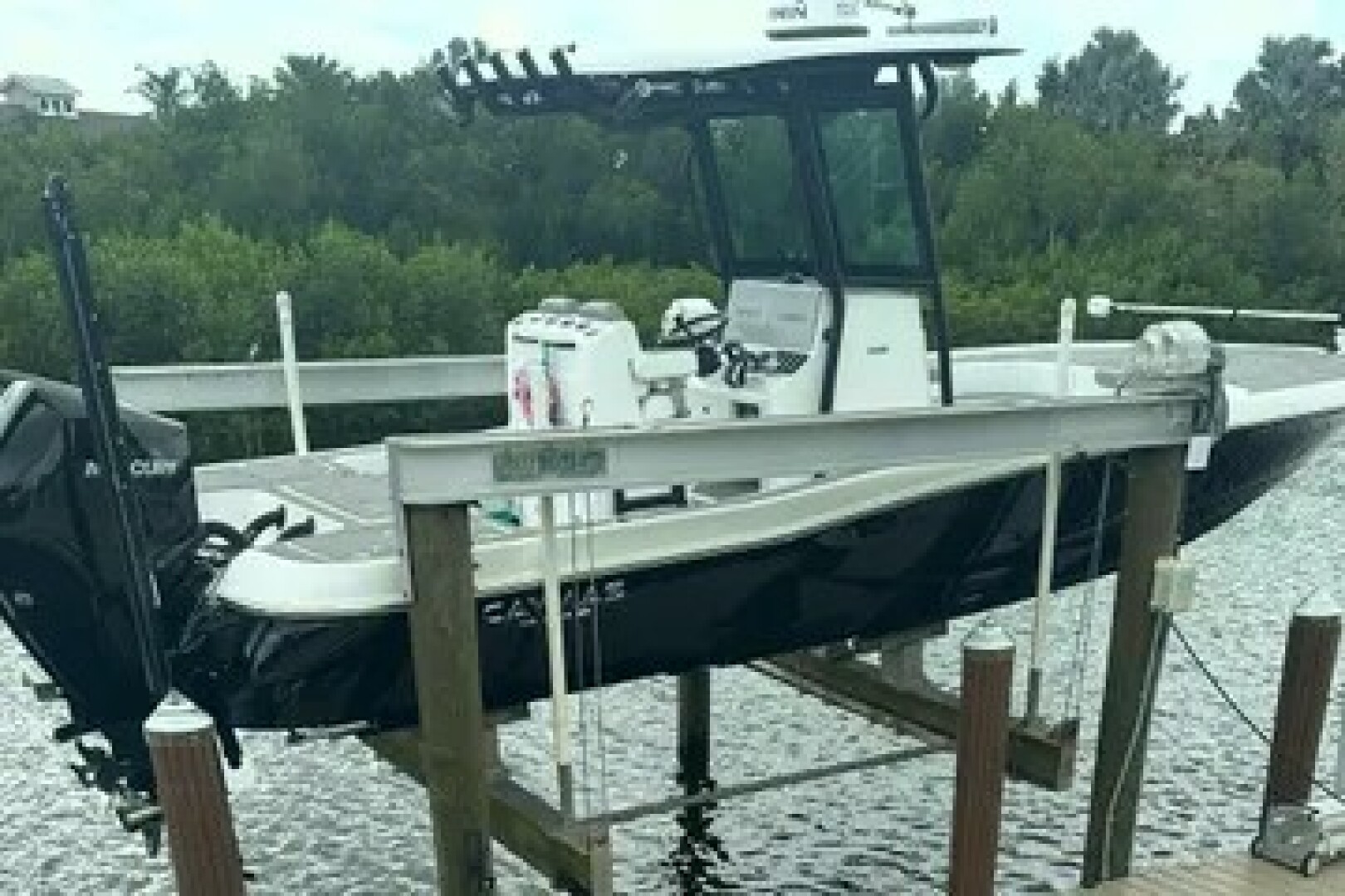 Slide: The Image of 2023 Caymas 28 HB Twin boat on lift, docked by lush greenery. - 5442523