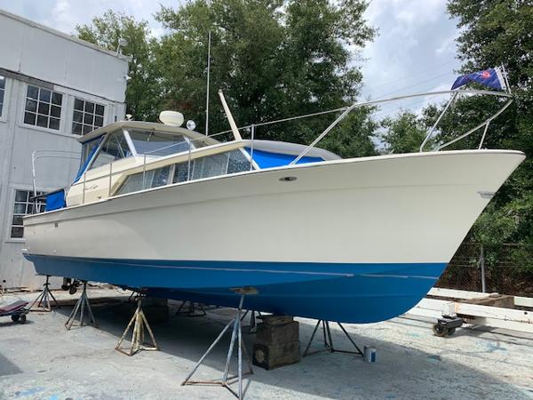 Slide: The Image of 1968 Chris-Craft 31 Commander boat on stands, white and blue hull, outdoor setting. - 1