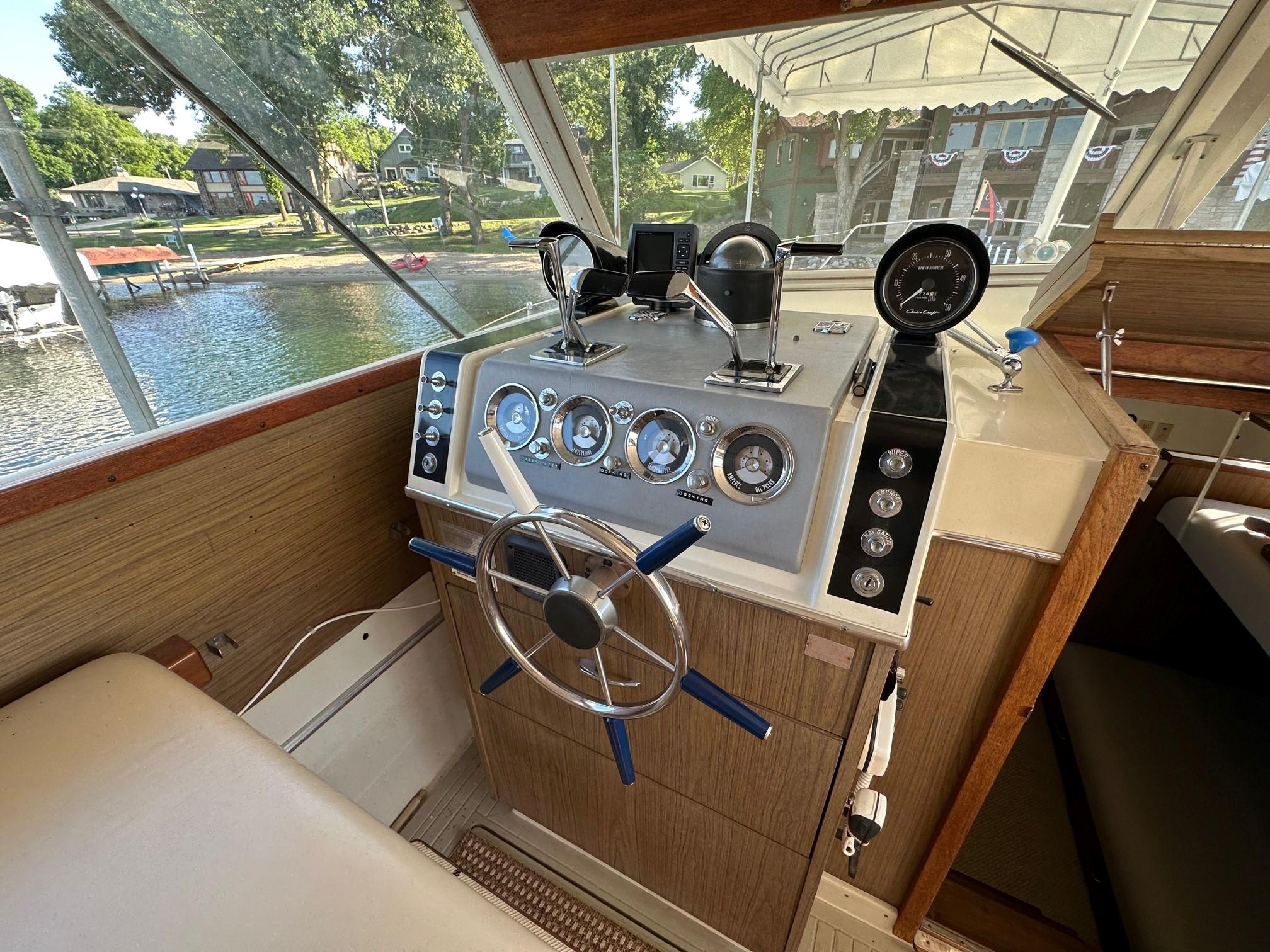 Slide: The Image of 1968 Chris-Craft 35 COMMANDER helm with classic gauges and steering wheel, docked by a lakeside. - 14
