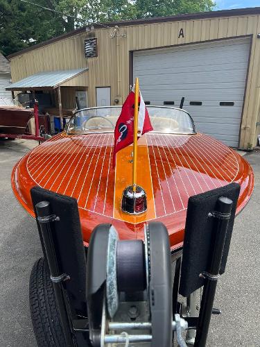 Slide: The Image of 1955 Chris-Craft Cobra 21 boat with wooden deck and flags, parked near a garage. - 2