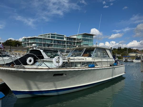Slide: The Image of 1969 Chris-Craft Commander boat docked at a marina with modern buildings in the background. - 1