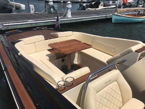 Slide: The Image of 2019 Chris-Craft Launch 34 boat interior with beige seating and wooden table at a marina. - 5