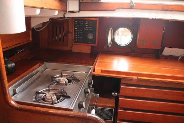 Slide: The Image of 1958 Concordia Yawl interior kitchen with stove, wooden cabinetry, and porthole window. - 10