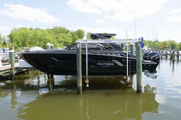 Slide: The Image of 2020 Cruisers Yachts 338 SS OB on lift at marina, black hull, calm water. - 0