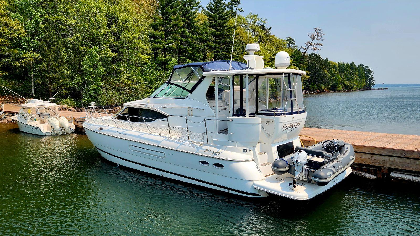 The Image of 2000 Cruisers Yachts 4450 docked by a scenic lakeside with lush greenery. - 0