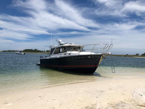 Slide: The Image of 2025 Cutwater C-32 Sedan boat anchored on sandy beach under blue sky. - 0