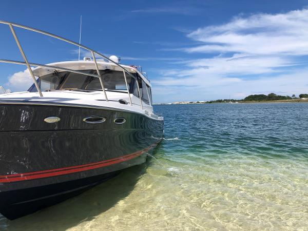Slide: The Image of 2025 Cutwater C-32 Sedan boat on clear water near sandy shore under blue sky. - 2