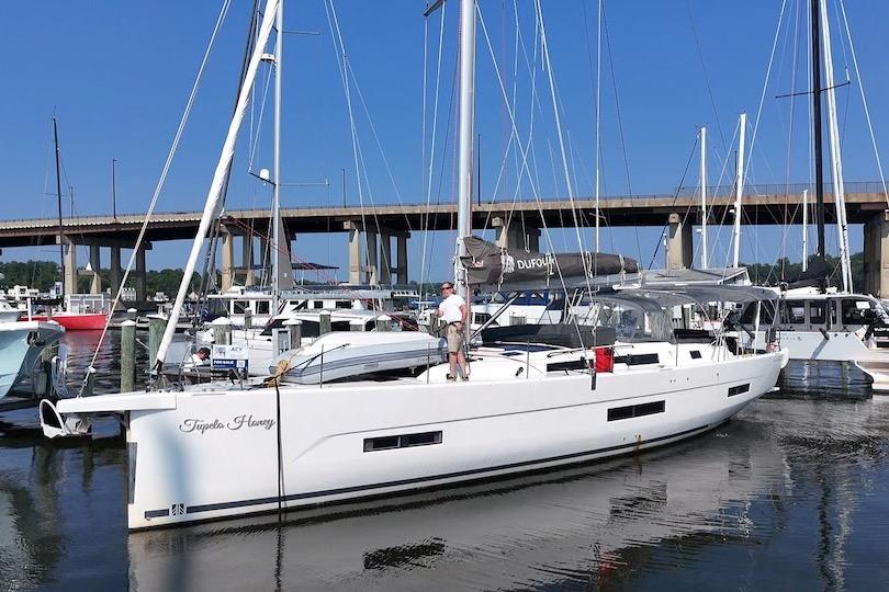 Slide: The Image of 2022 Dufour 530 sailboat docked at marina, clear blue sky, bridge in background. - 1