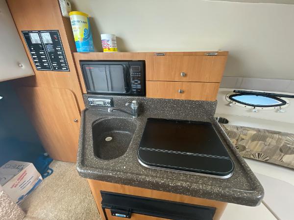 Slide: The Image of 2009 Glastron GT 249 boat interior kitchen with sink, microwave, and storage cabinets. - 13