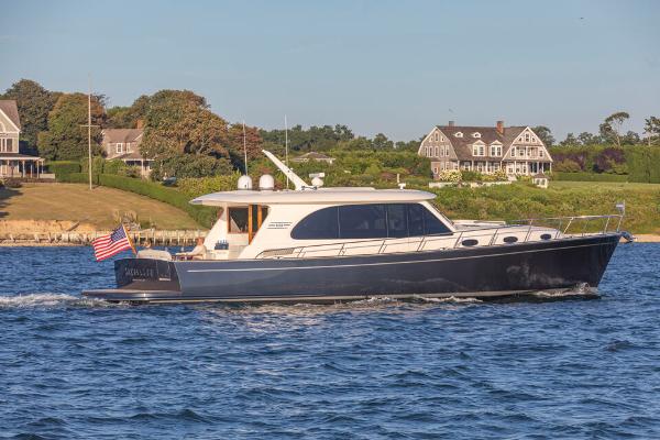 Slide: The Image of 2023 Eastbay EB60 yacht cruising near coastal homes, American flag displayed. - 28