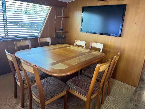 Slide: The Image of Dining area in 1986 Hatteras 70' Cockpit Motor Yacht with wooden table, chairs, and wall-mounted TV. - 20