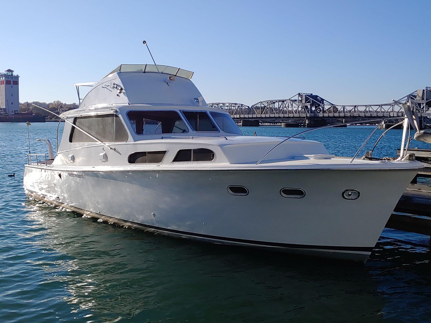 Slide: The Image of 1961 Hatteras Convertible yacht docked near a bridge on a sunny day. - 0