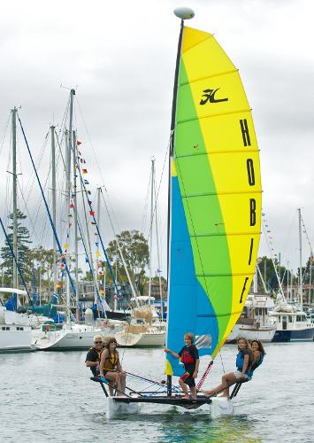 Slide: The Image of 2023 Hobie Cat Getaway sailboat with colorful sail on the water, marina background. - 5