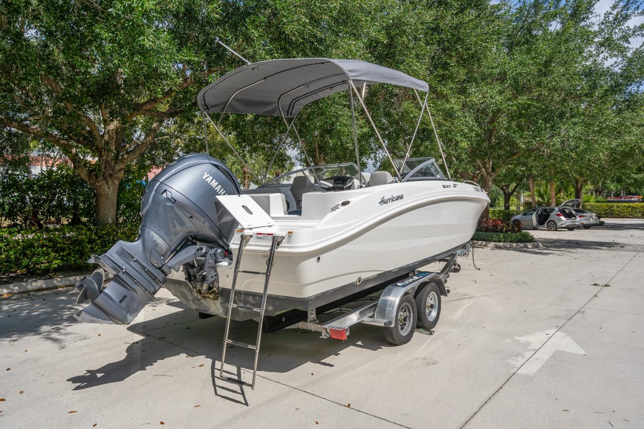 Slide: The Image of 2025 Hurricane SunDeck 217 OB boat on trailer, parked outdoors with trees in background. - 3
