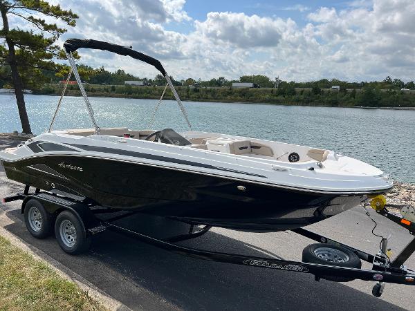 Slide: The Image of 2024 Hurricane SunDeck Sport 205 IO boat on a trailer by a lake. - 1