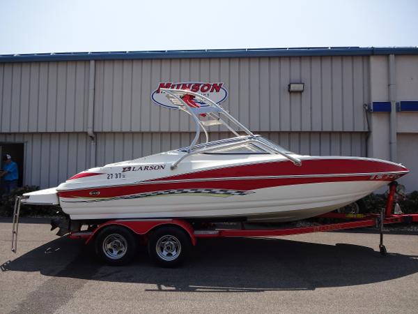 Slide: The Image of 2007 Larson 206 Senza boat on trailer, red and white design, parked outside a building. - 1