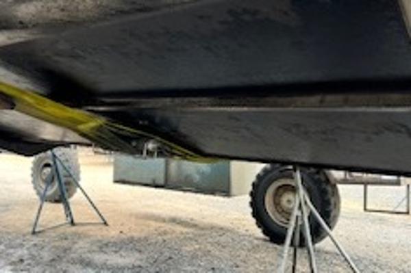 Slide: The Image of 2003 Larson 330 CABRIO boat underside on stands, with visible trailer wheels. - 34