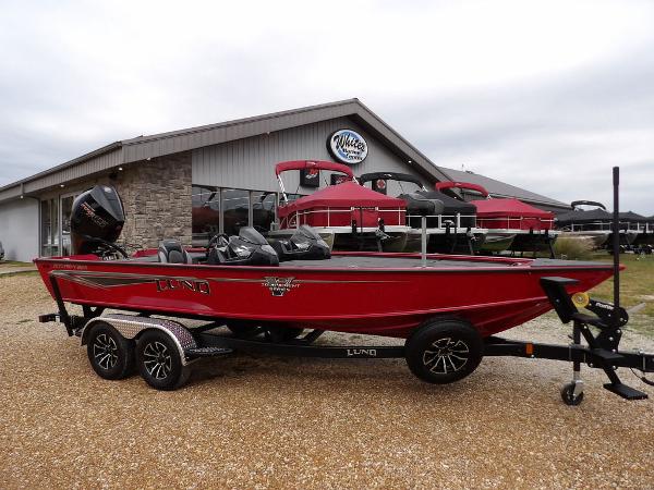 Slide: The Image of 2024 Lund 2075 Pro-V Bass XS boat in red on a trailer outside a dealership. - 1