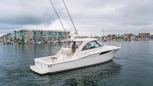 Slide: The Image of 2023 Mag Bay 42 Express yacht cruising in a marina with modern buildings in the background. - 16