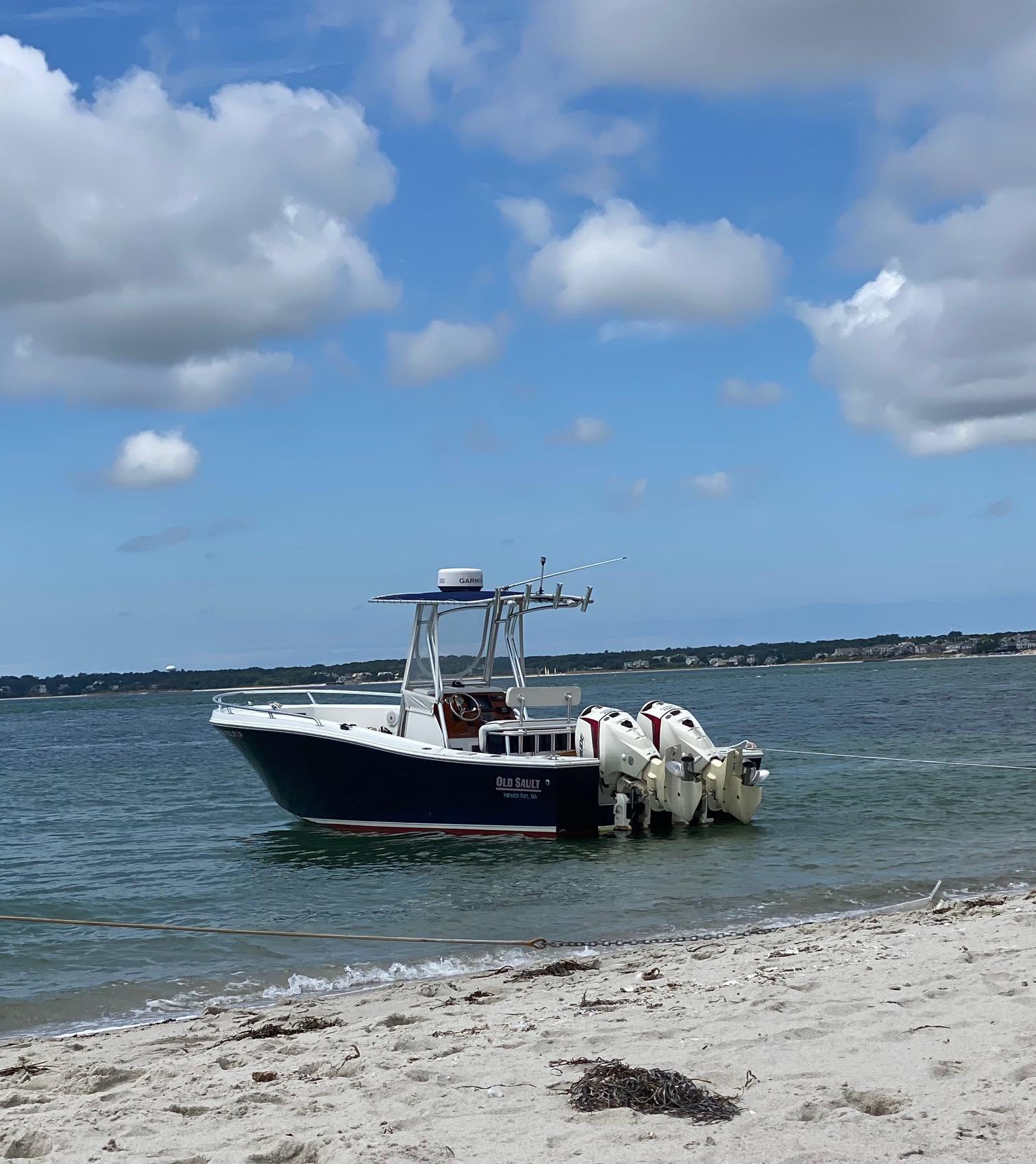 Slide: The Image of A 1991 Mako 241 boat anchored near a sandy beach under a partly cloudy sky. - 2