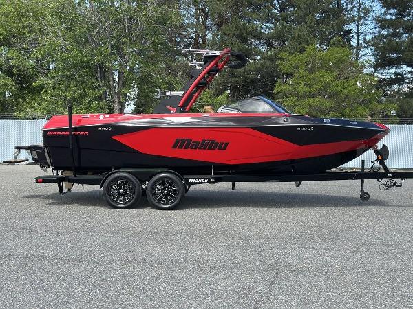 Slide: The Image of 2025 Malibu 23 LSV boat in red and black on a trailer, parked outdoors. - 0